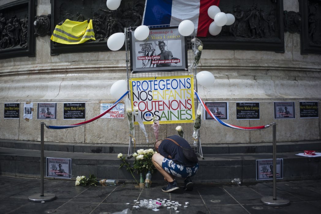 A man lights up a candle on Republique square as a sign is seen reading "Protect our children, support our elders" during a demonstration in Paris against police violence and the death of 24-year-old Steve Maia Canico, on Saturday, Aug. 3, 2019. The western French city of Nantes on Friday imposed exceptional security measures amid growing public anger over the drowning of a local man following a violent clash between police and people attending a music festival. (AP Photo/Kamil Zihnioglu)