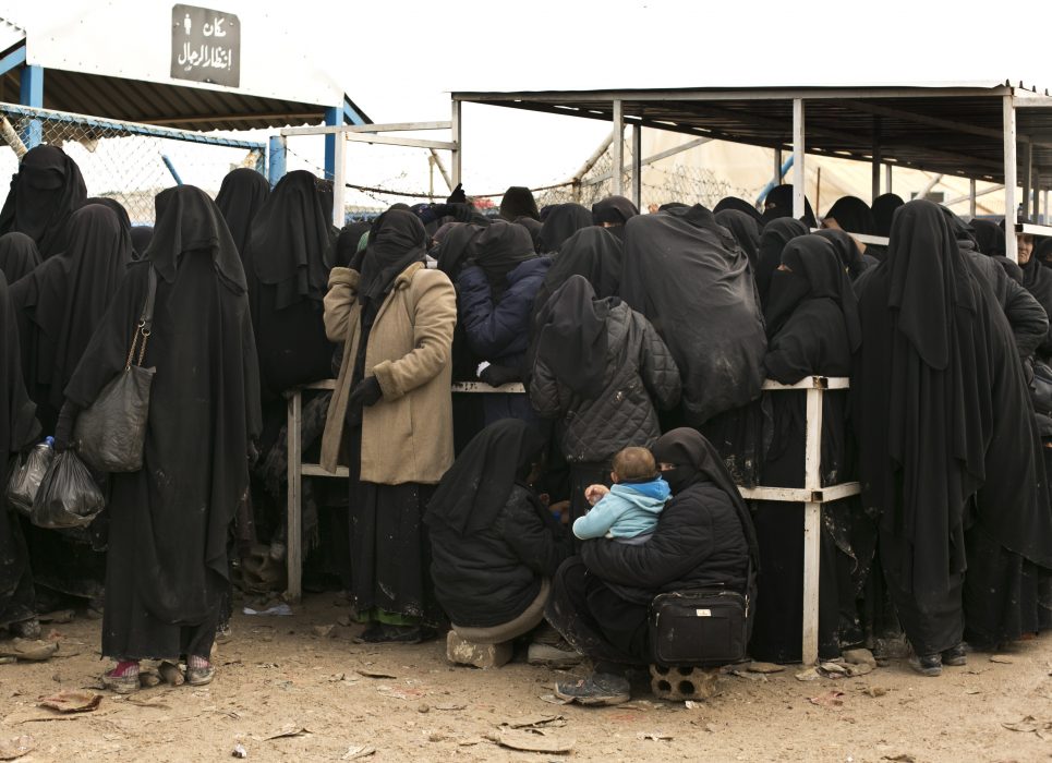 In this Sunday, March 31, 2019 photo, a woman waits with her baby for aid supplies at Al-Hol camp, in Hassakeh province, Syria. An international aid group says it recorded 31 deaths in the final week of March among people making their way out of the last sliver of territory held by the Islamic State group and toward a camp for the displaced. The International Rescue Committee says Monday the highest weekly death rate reflects the desperate conditions of the mostly women and children who left the village of Baghouz for al-Hol camp. The IRC figures could not be independently confirmed. (AP Photo/Maya Alleruzzo)
